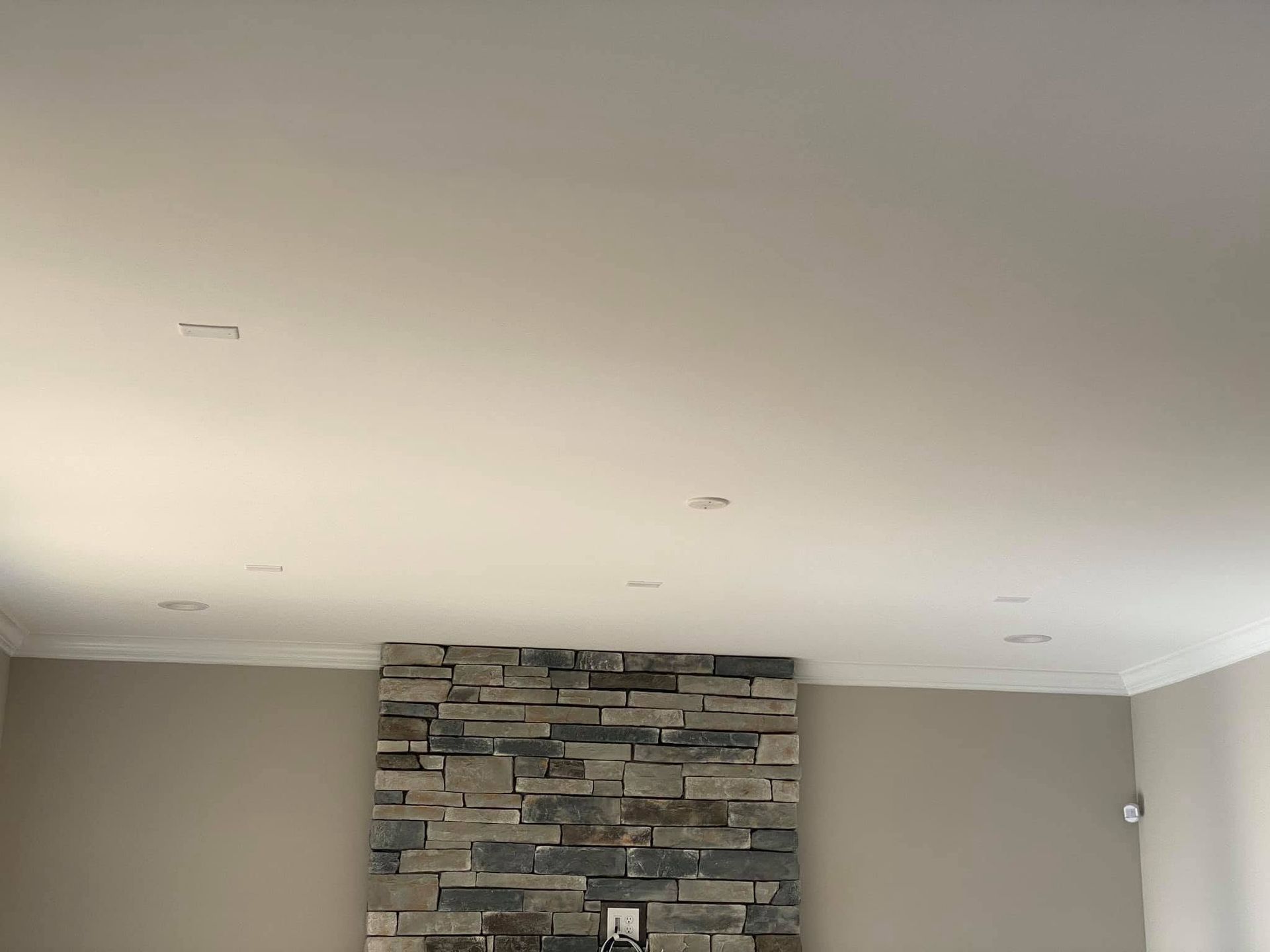 Living room ceiling with recessed lights and a stone accent wall below.