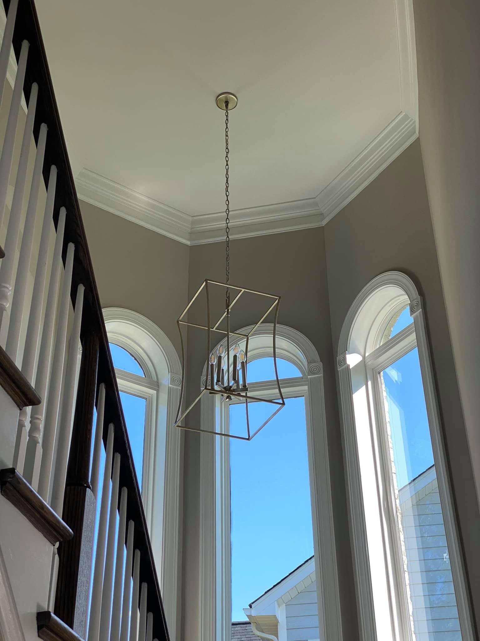 Tall arched windows and a hanging geometric chandelier in a bright stairwell nook