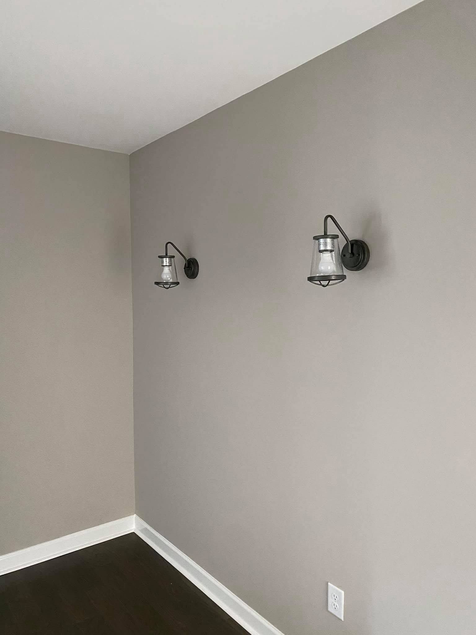Empty gray room corner with two wall sconces and a white electrical outlet.