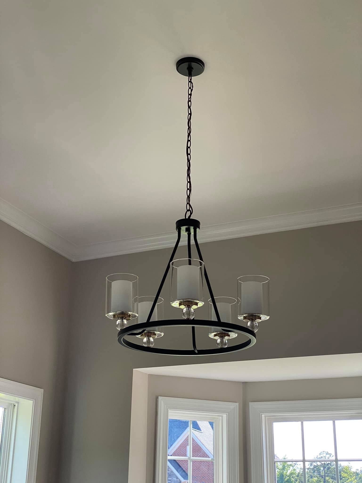 Black metal chandelier hanging from a white ceiling above windows.