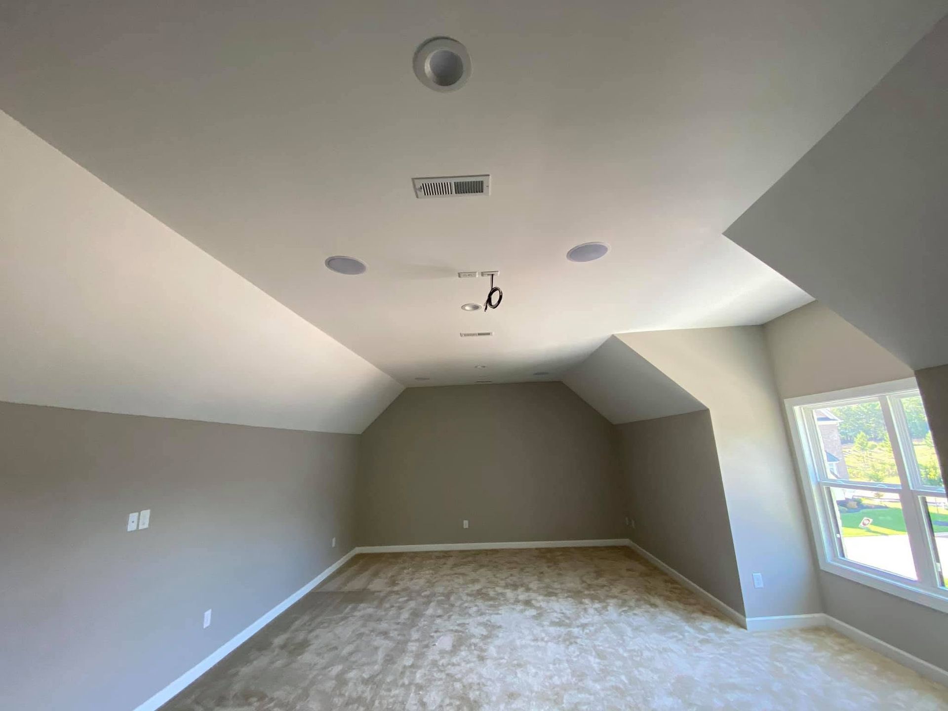 Empty gray bedroom with vaulted ceiling, recessed lights, carpet, and a window on the right