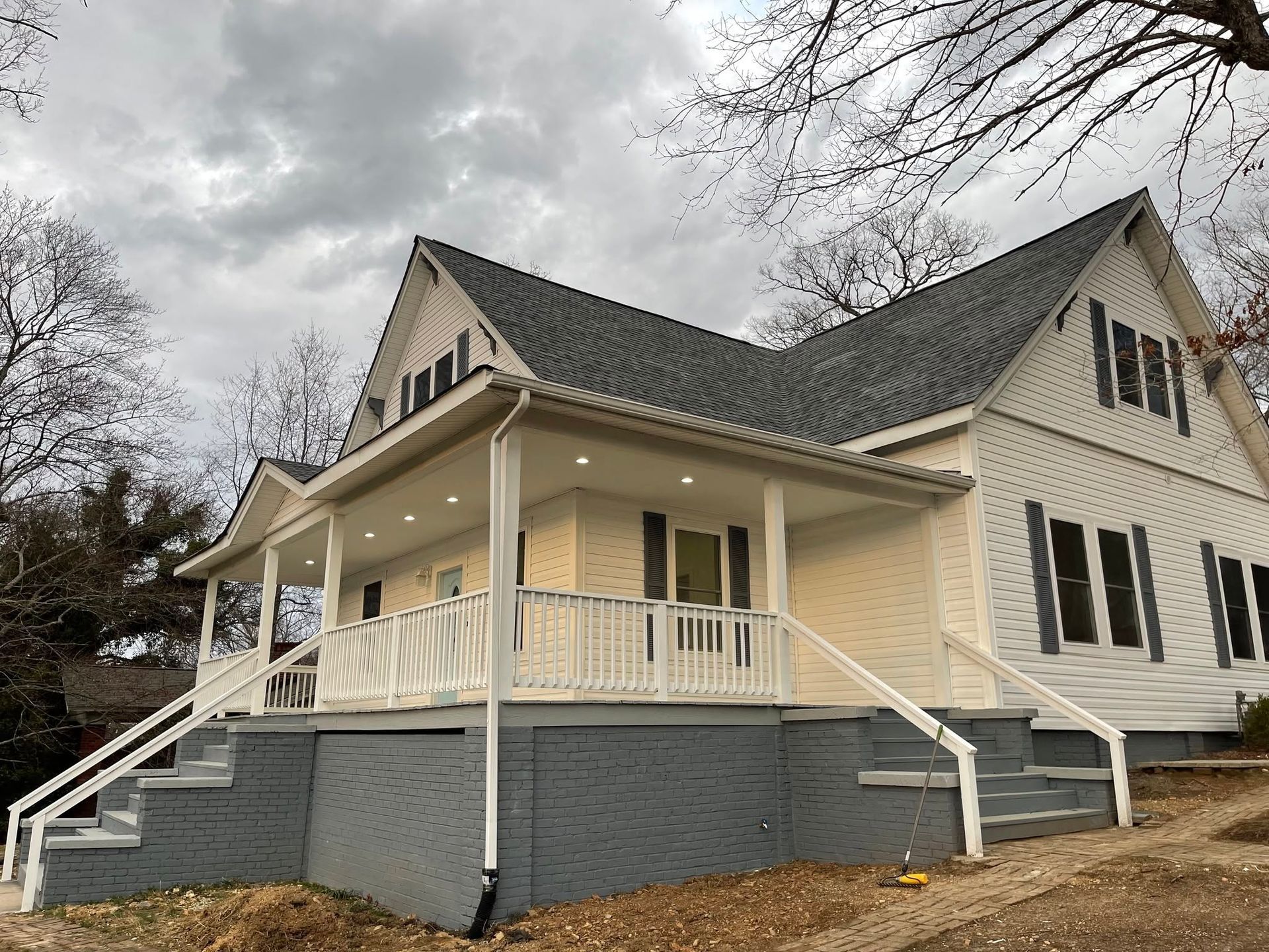 Cream-colored house with a wraparound porch and gray roof on a cloudy day