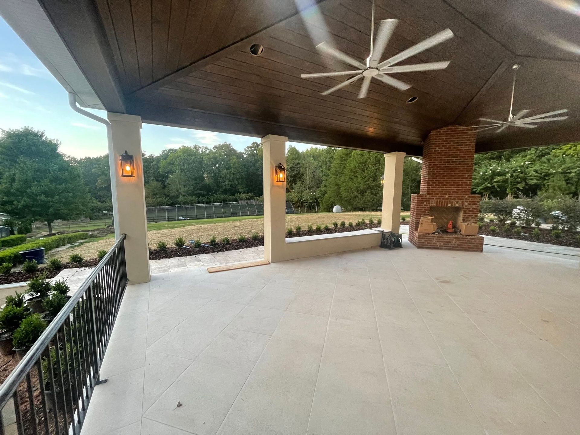 Covered patio with ceiling fans, brick fireplace, and open view to landscaped garden and trees
