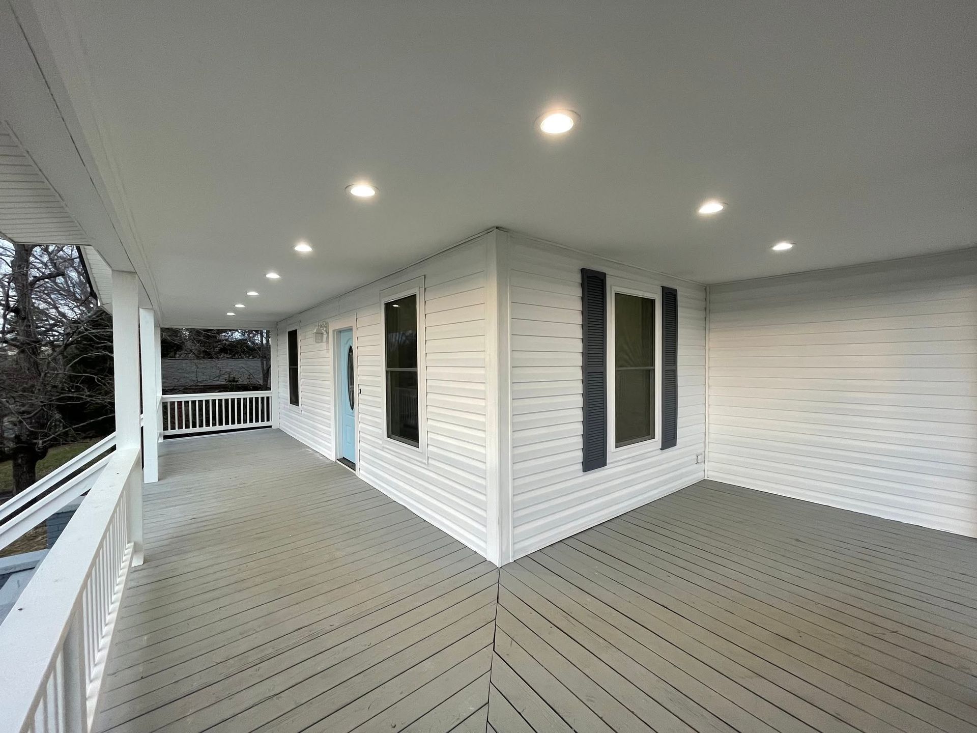 Covered porch with gray flooring, white siding, ceiling lights, and black shutters.