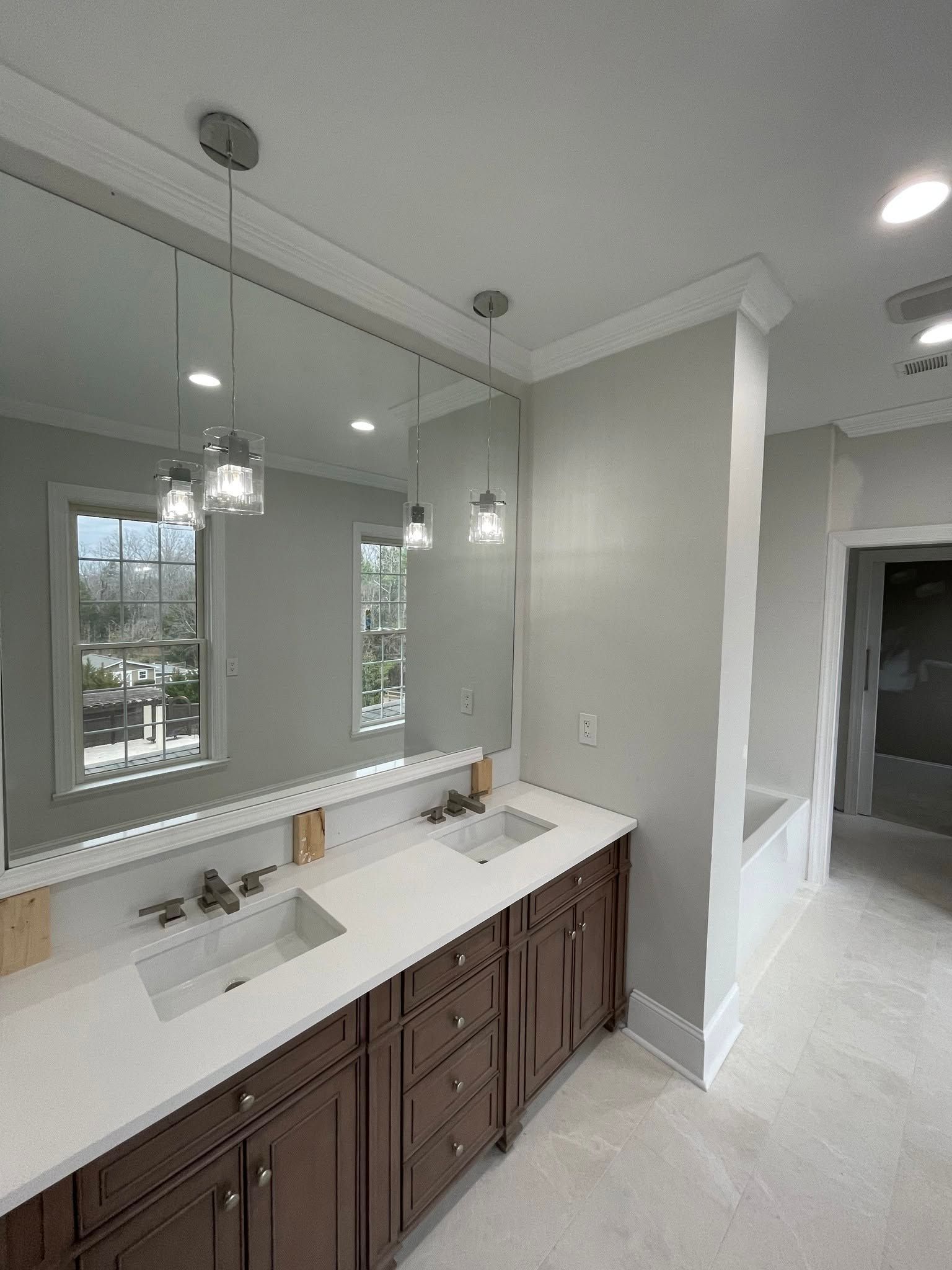 Bright bathroom vanity with double sinks, large mirror, pendant lights, and gray walls overlooking windows