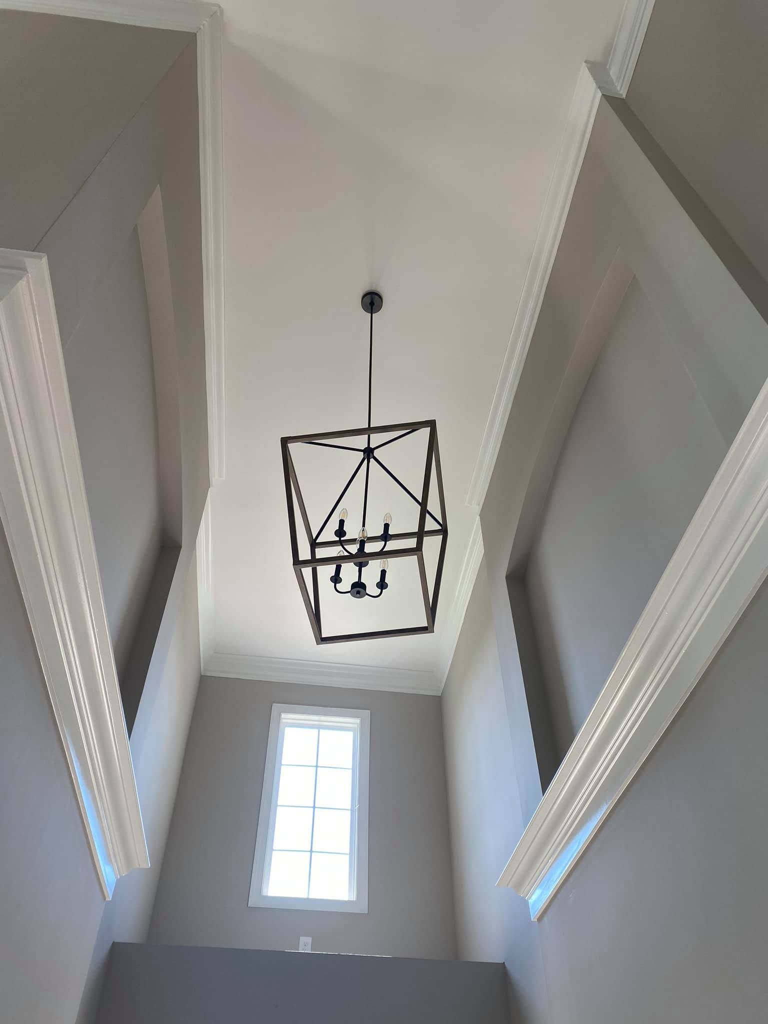 Tall hallway ceiling with a hanging black lantern and a bright window below.