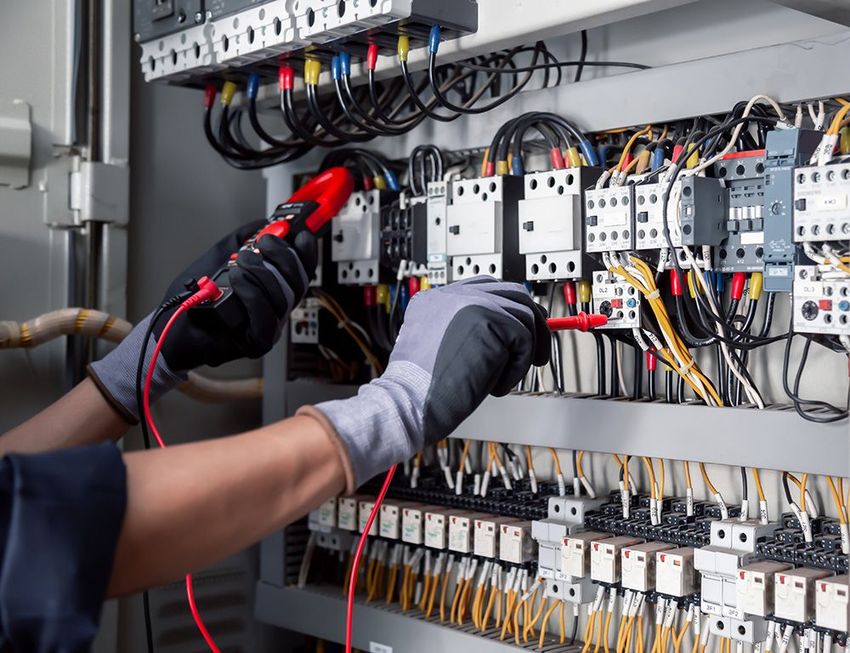 Technician testing an electrical control panel with red and black probes
