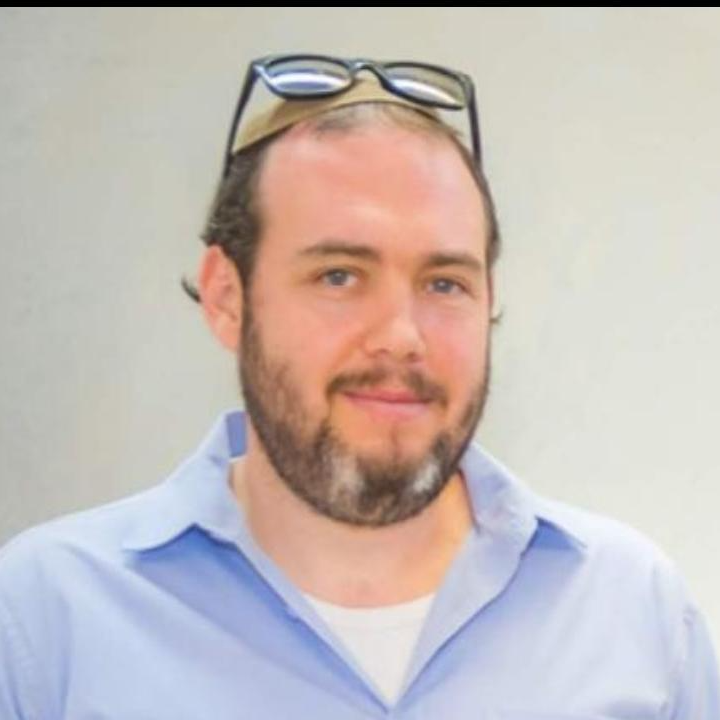 גבר עם משקפיים על הראש, מביט למצלמה. הוא לובש חולצה כחולה מכופתרת.