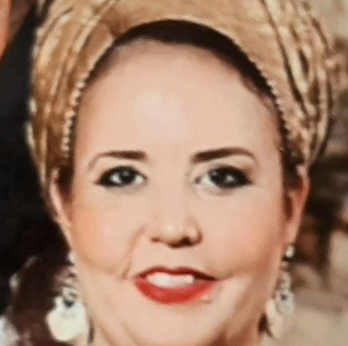 אישה עונדת כיסוי ראש עם דוגמאות ועגילים, מחייכת עם שפתון אדום.