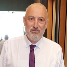 גבר עם זקן בחולצה לבנה ועניבה סגולה, בתוך הבית.