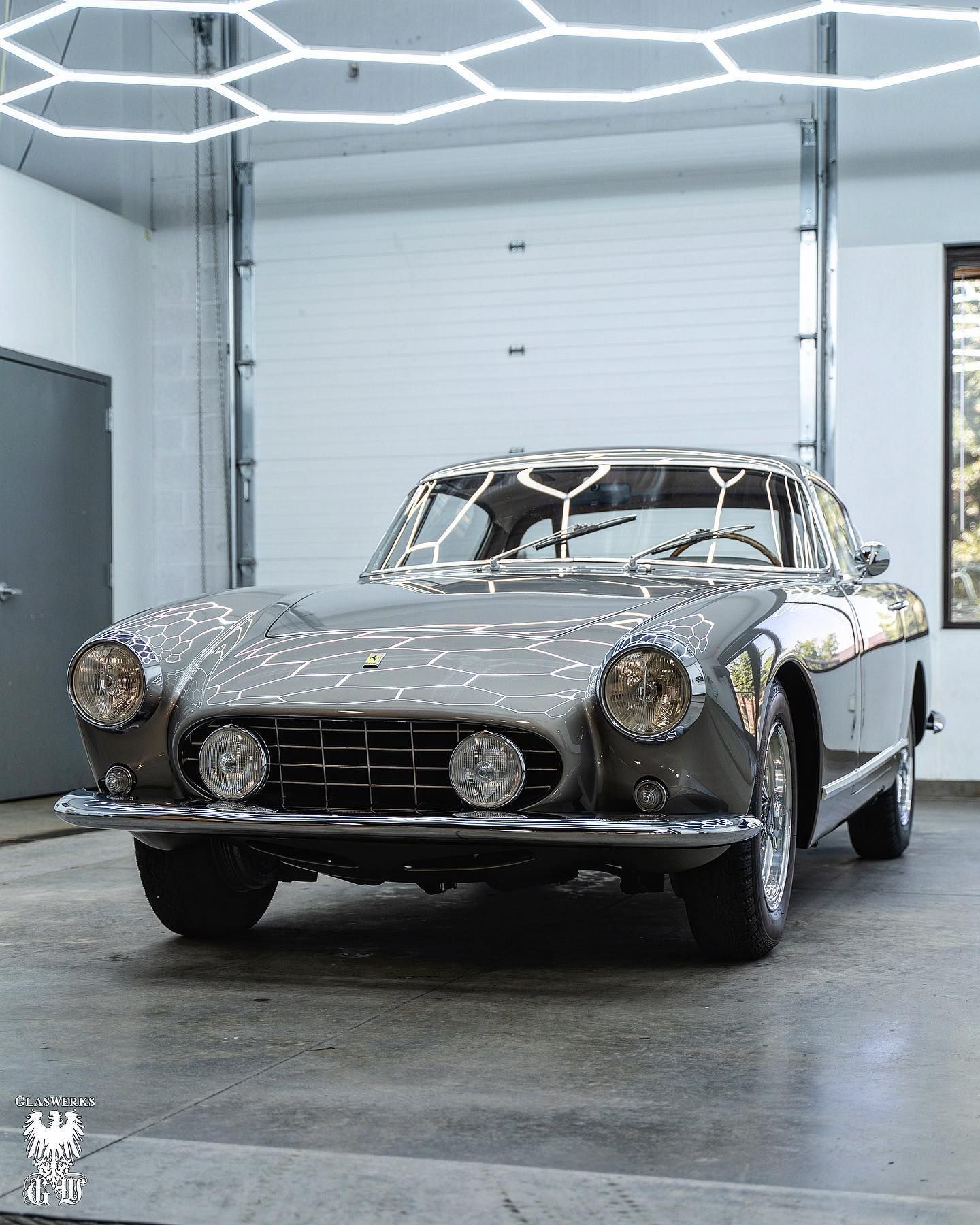Classic silver sports car parked in a modern garage under bright geometric ceiling lights