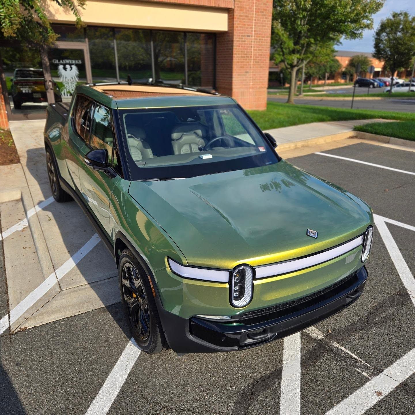 Green Rivian SUV parked in a lot, front view near a building.