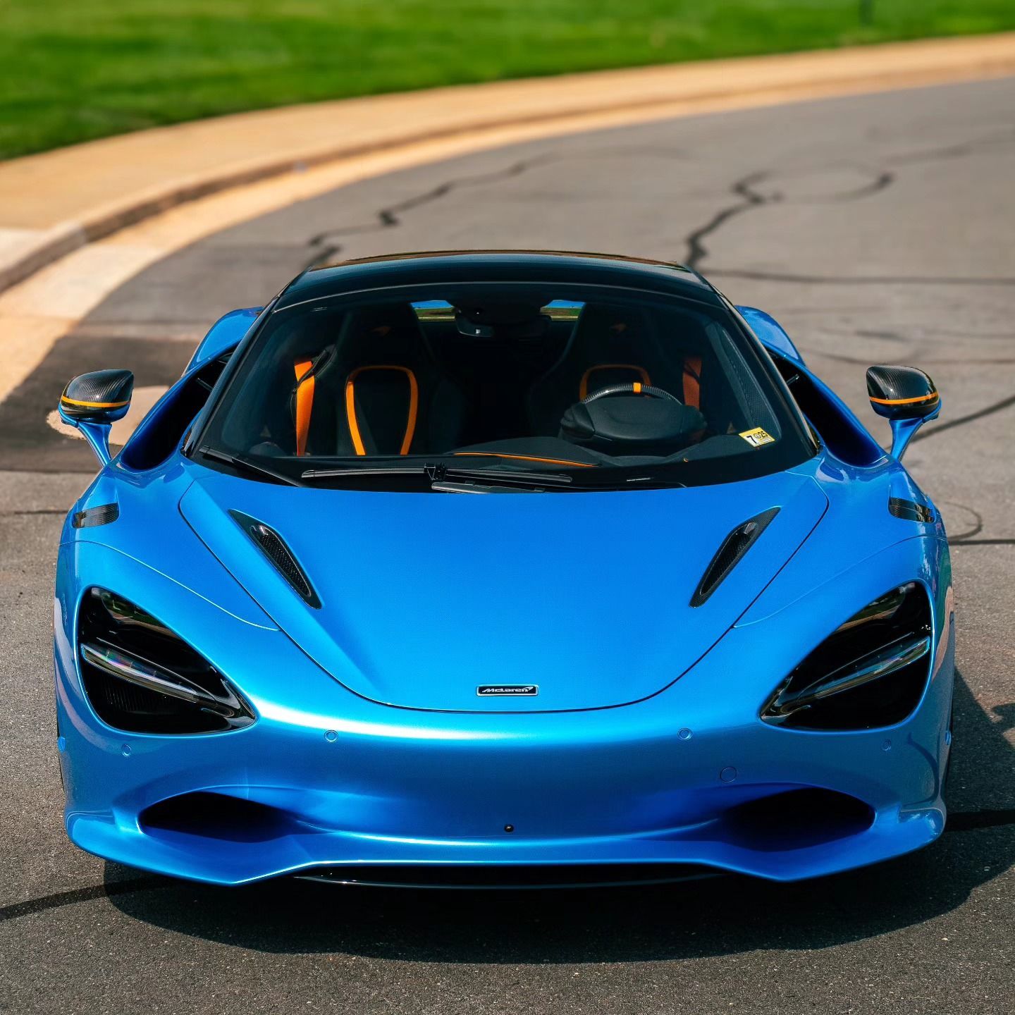 Blue sports car on a curved road, front view with black accents and orange interior.