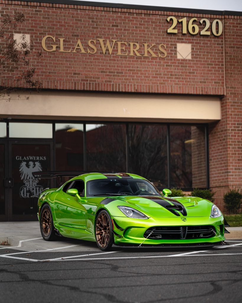 A green sports car is parked in front of a glassworks building.