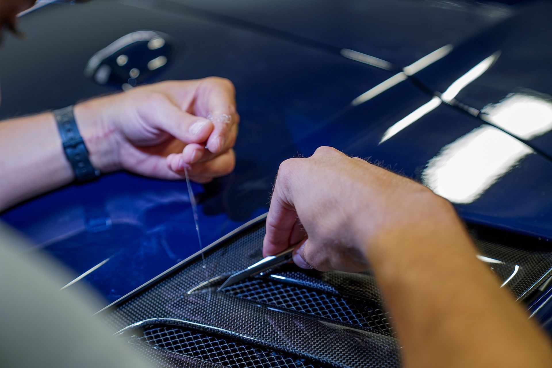 Hands pulling protective film from a glossy black car hood at a detailing workshop