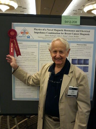 Elderly man in beige jacket standing beside a research poster at a conference, smiling and holding a red ribbon
