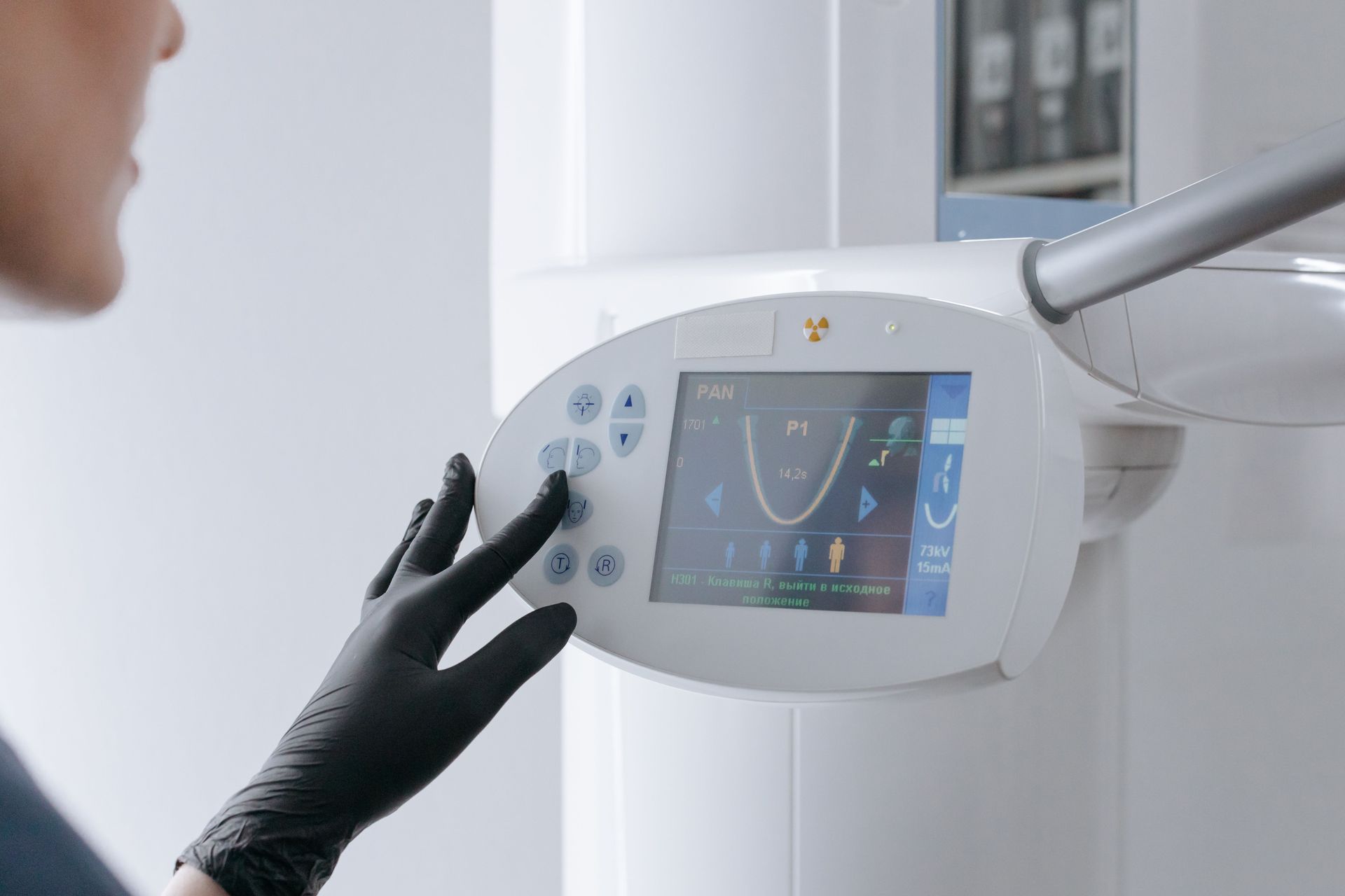 Gloved hand operating a dental X-ray machine control panel in a clinic