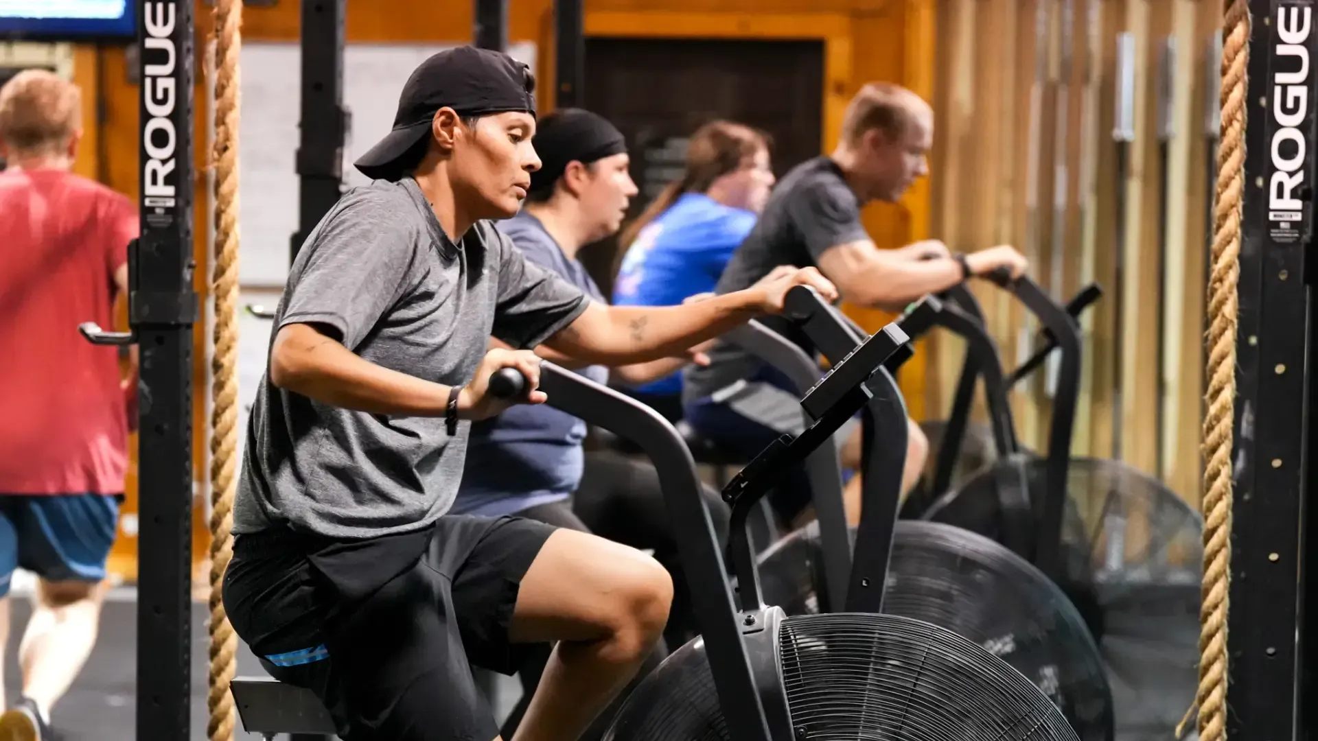 People exercising on air bikes in a gym in Morgantown, WV, with a Rogue rack in the background.