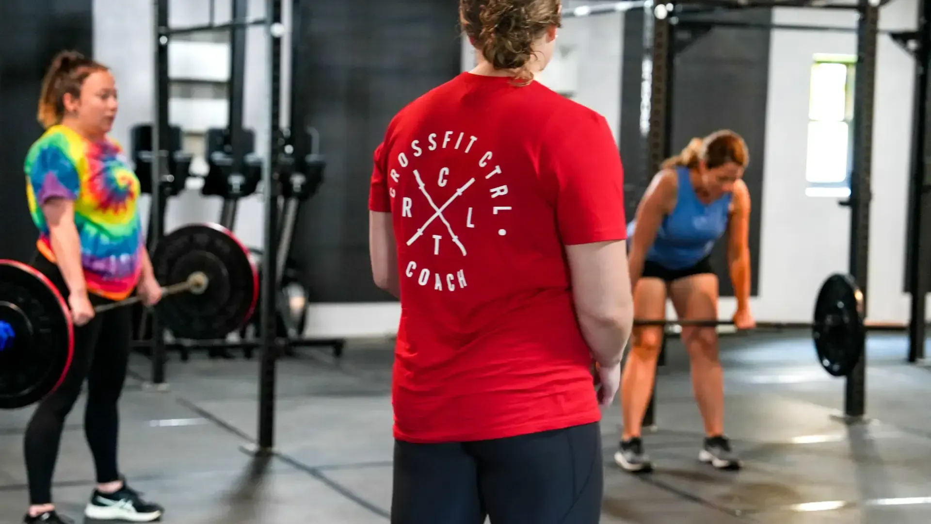 People working out in a gym in Morgantown, WV, with one person lifting a barbell and others preparing exercises.