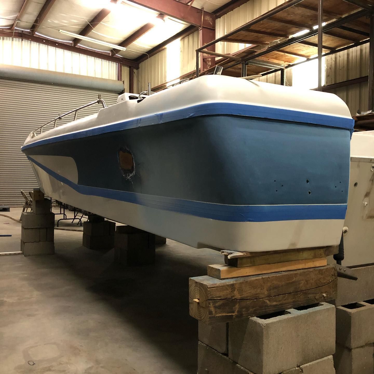Blue-and-white boat hull on wooden blocks inside a warehouse or workshop