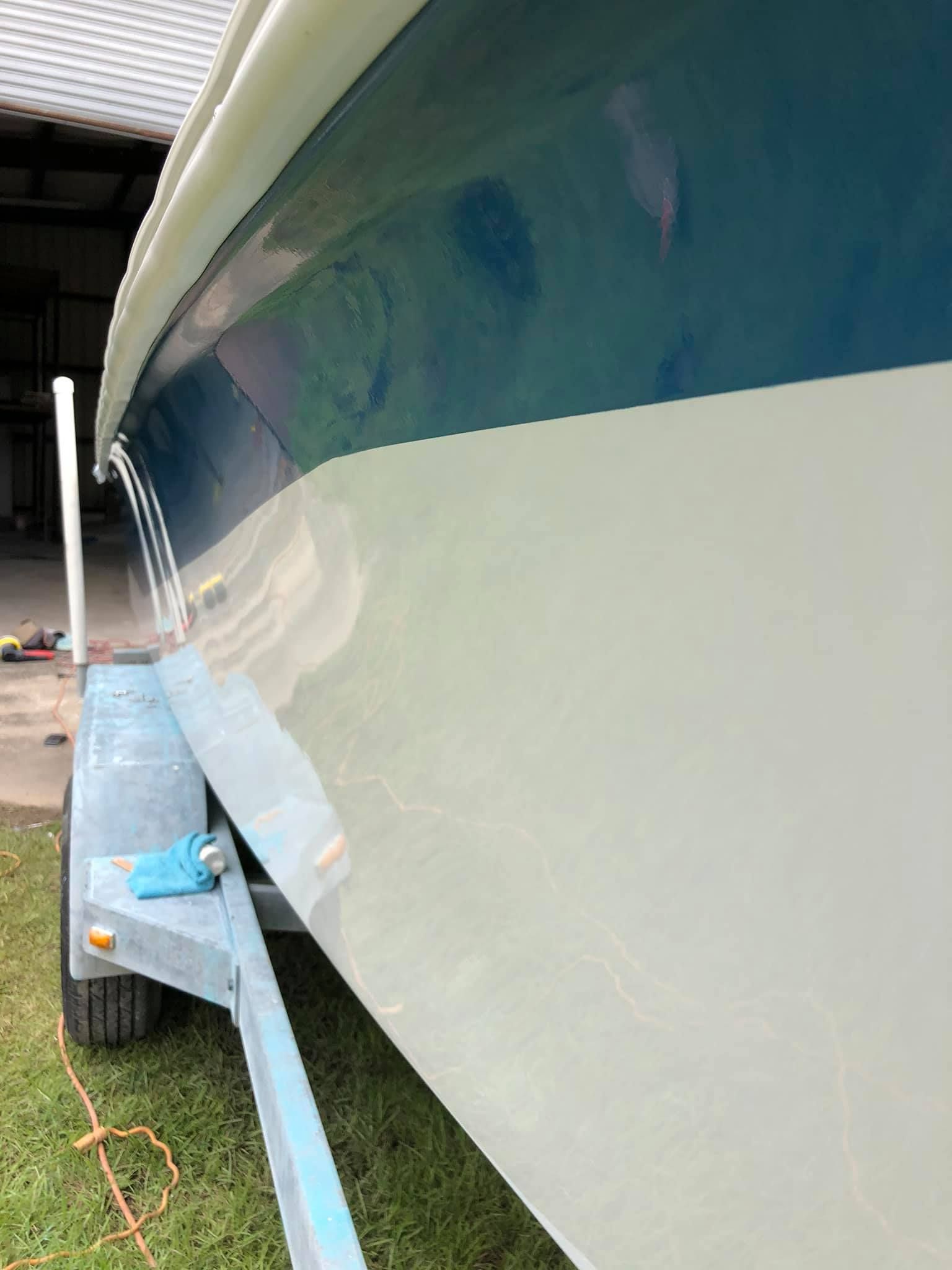 Boat hull on a trailer, white and blue, viewed from the side in a garage or boathouse.