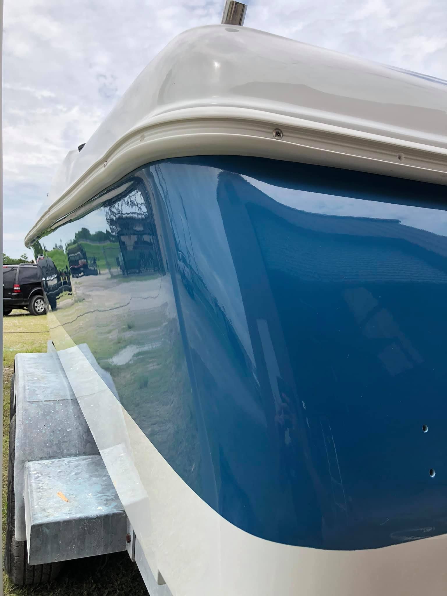 Close-up of a blue and white boat cabin window with a reflective windshield on a grassy shore
