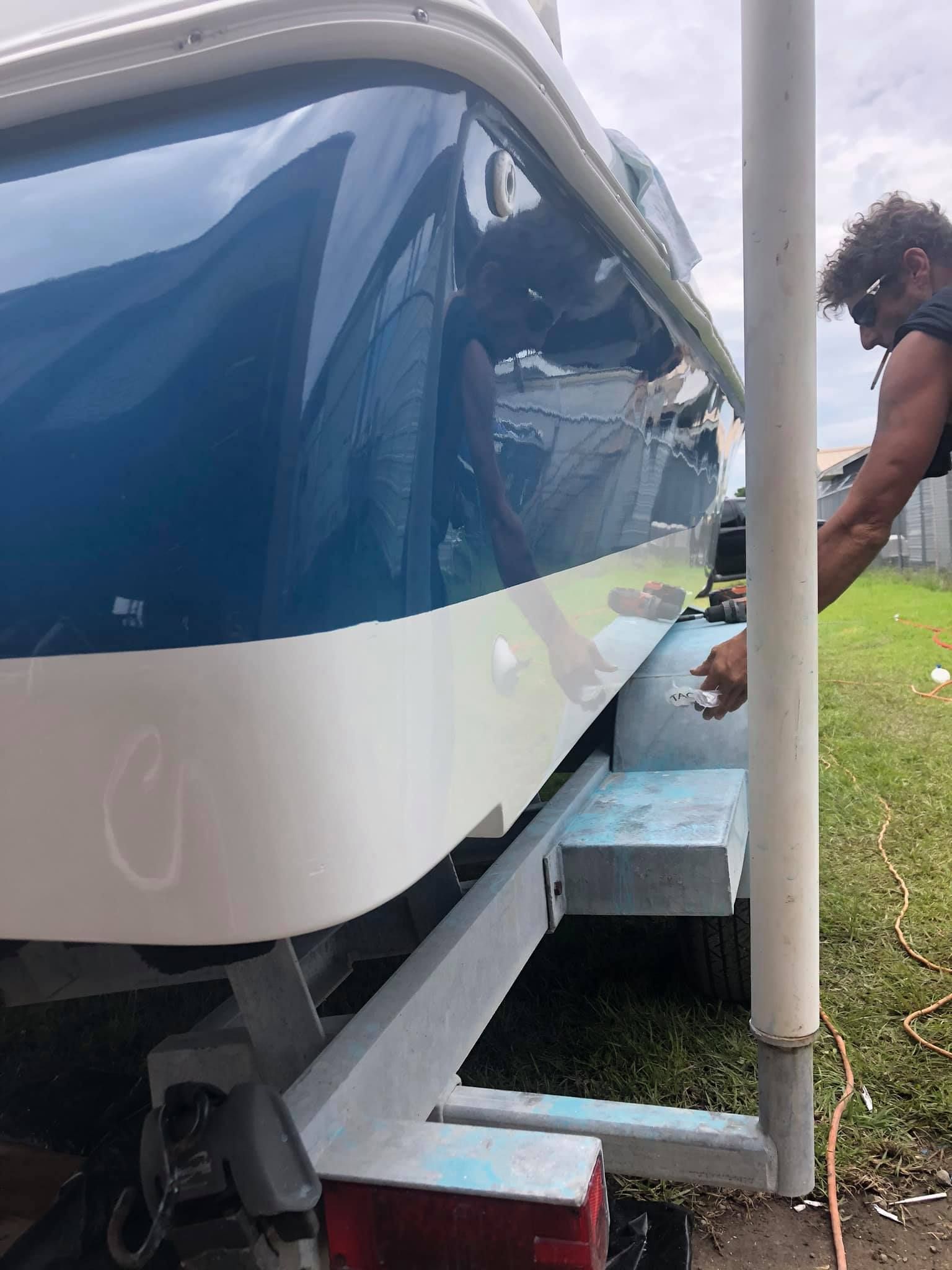 Boat with blue canopy being secured to a trailer beside a roadside pole.