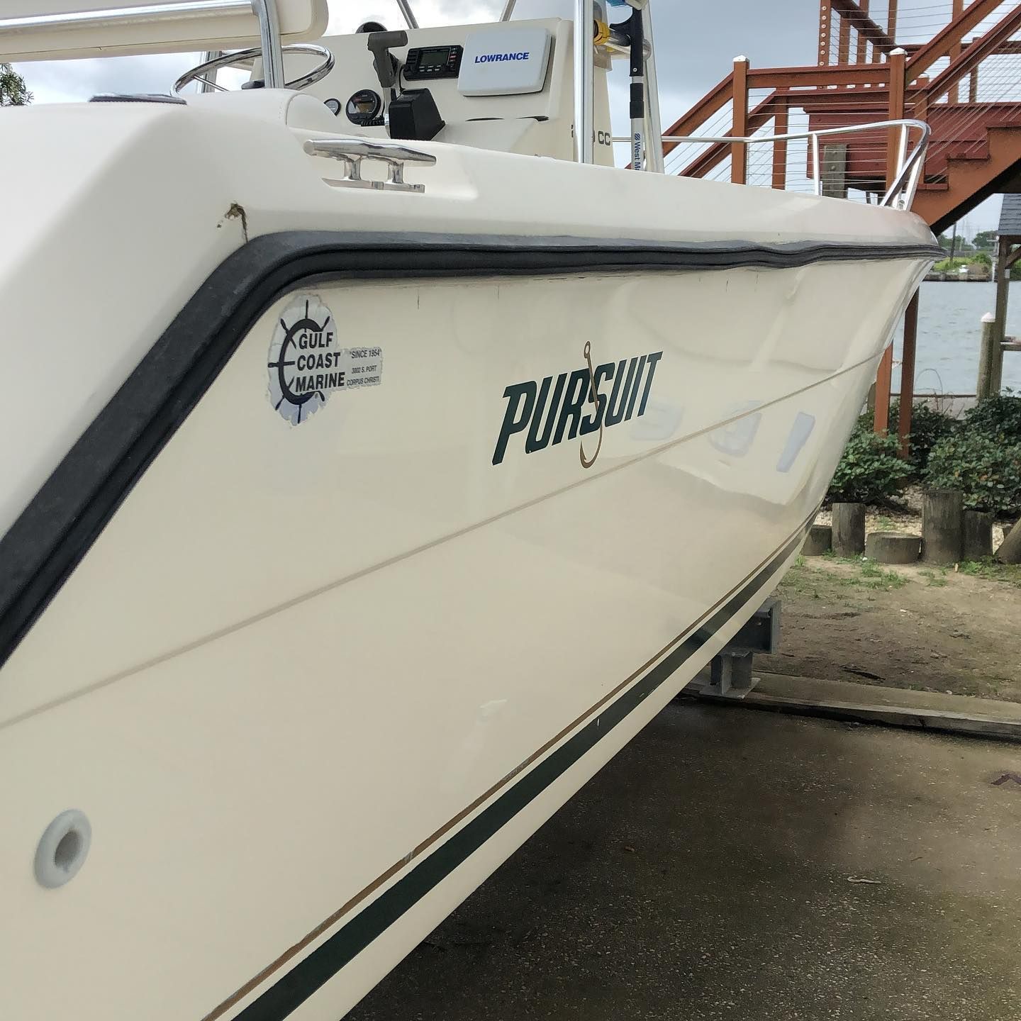 White boat bow with black trim docked beside a wet concrete pier, marina background