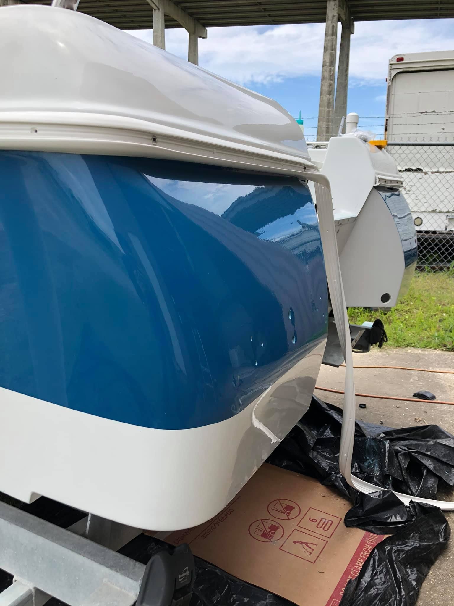 Blue and white boat hull propped on supports, with damaged debris underneath in a covered outdoor area
