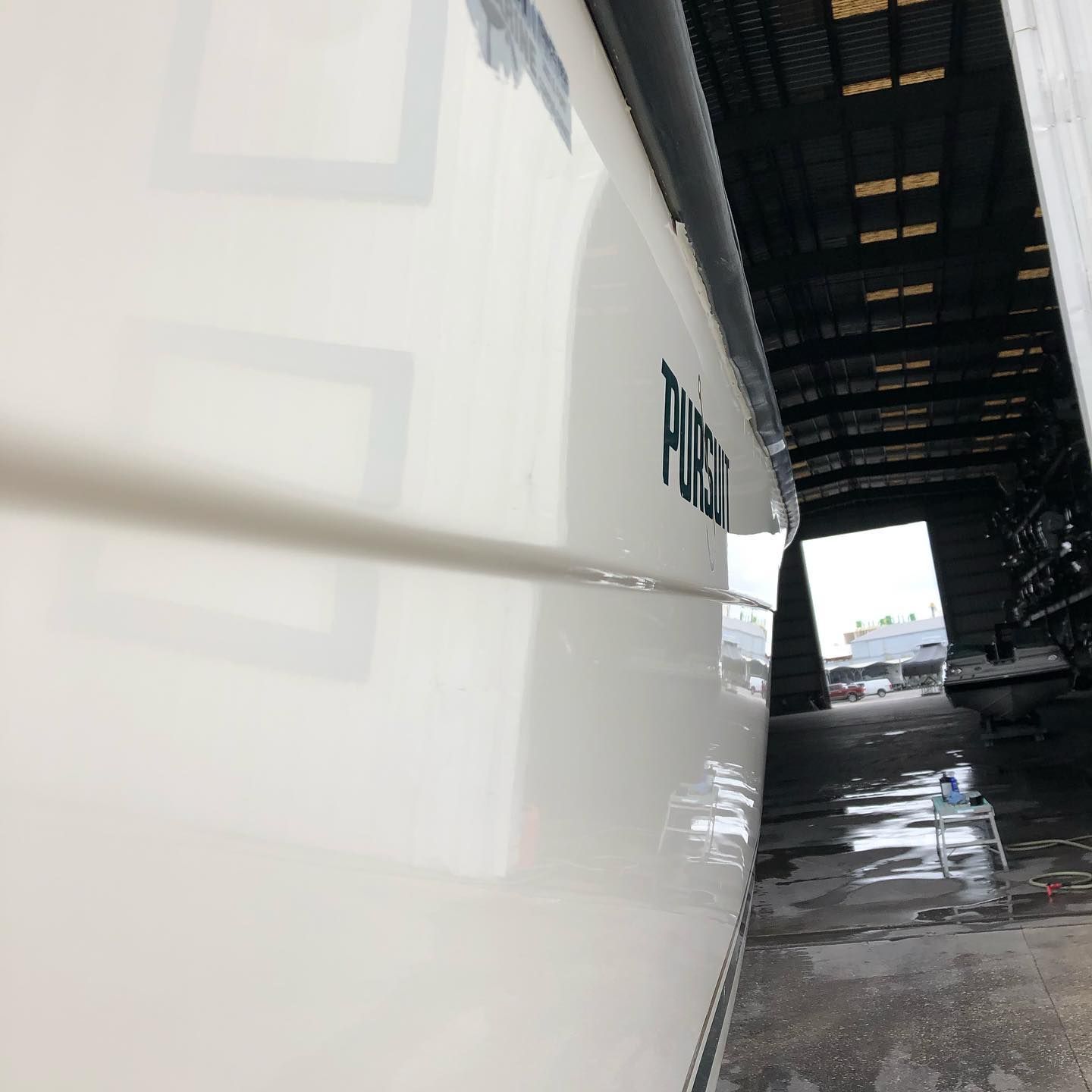 Close-up of a white bus under a covered depot, with wet pavement and an open roadway in the distance