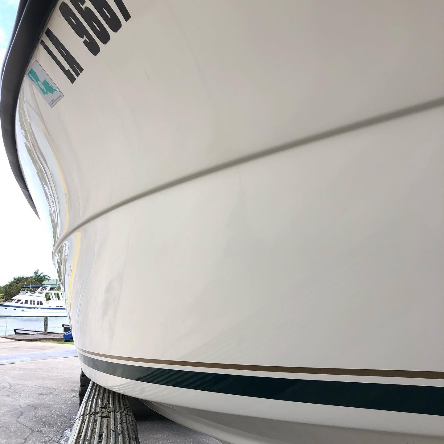 Close-up of a white boat hull with teal and brown trim at a marina.