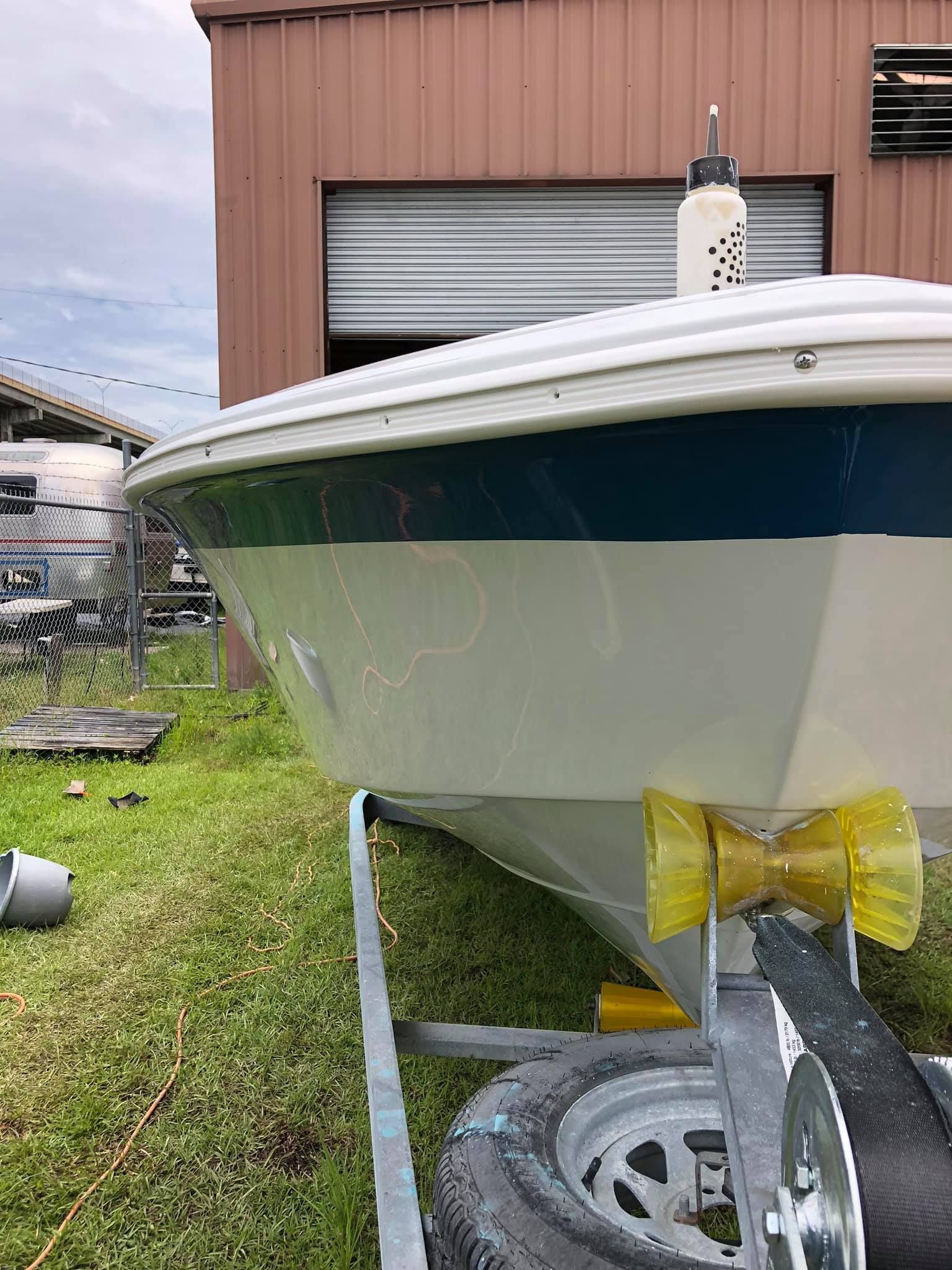 White boat on trailer in grassy yard beside a pink metal building