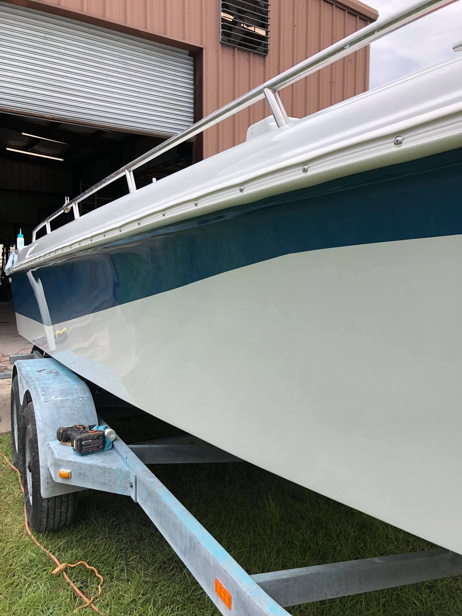 White boat on a trailer in a warehouse, side view with blue stripe and railings