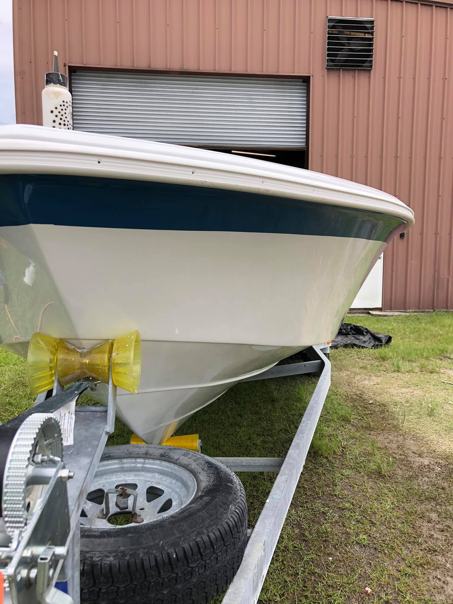White boat on trailer parked on grass beside a pink metal building