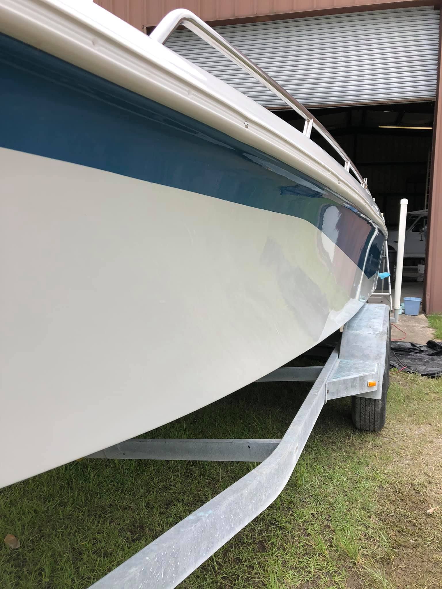 White boat on a trailer under a shed, with a blue stripe along the hull.