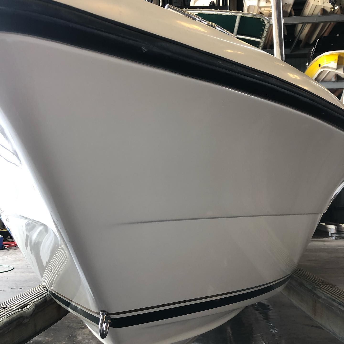 Close-up of a white boat hull with black trim in a workshop or marina setting
