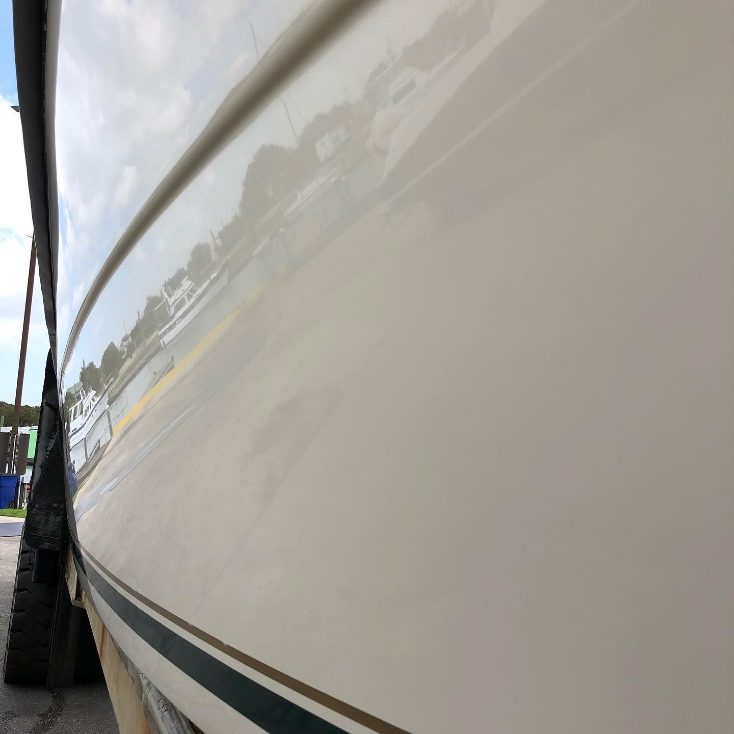 Close-up of a white boat hull with a dark stripe, reflecting the dock and surroundings
