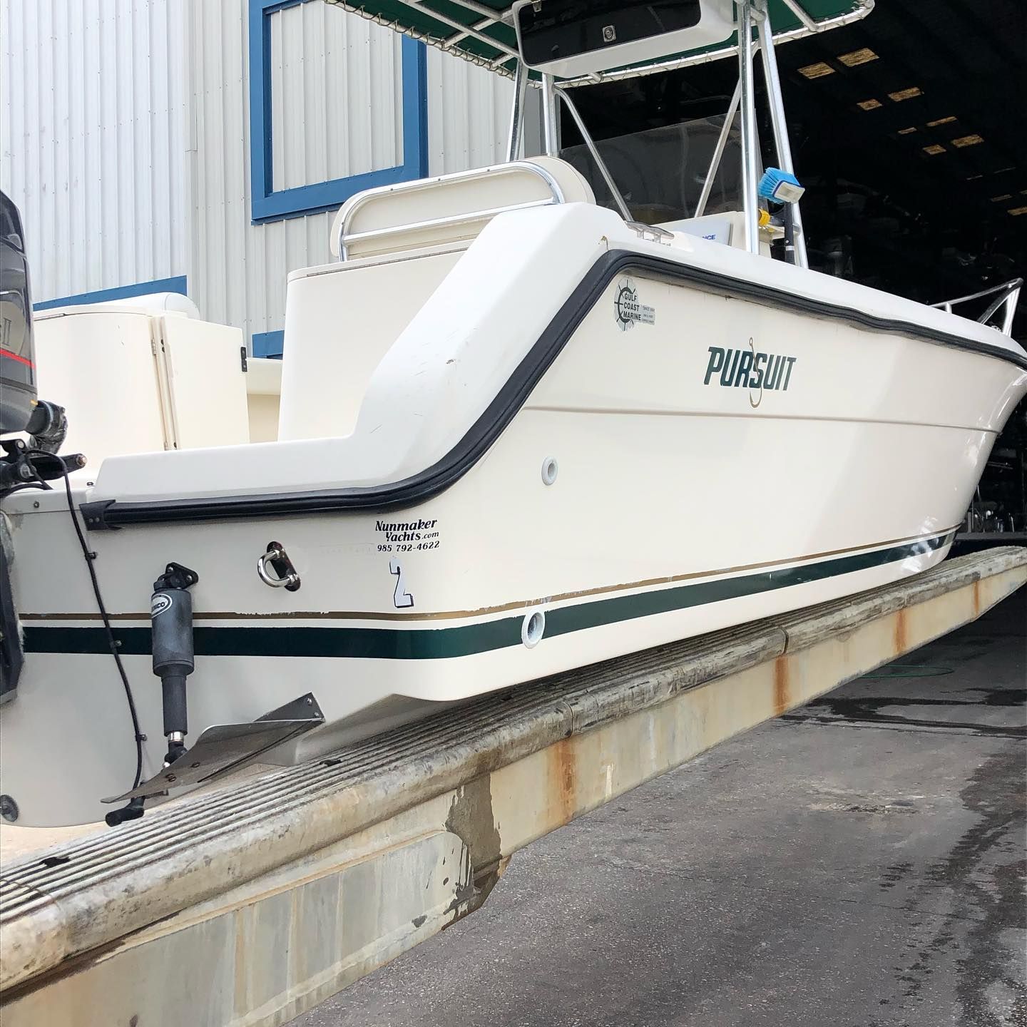 White fishing boat on a trailer at a dockside boat ramp near a warehouse.
