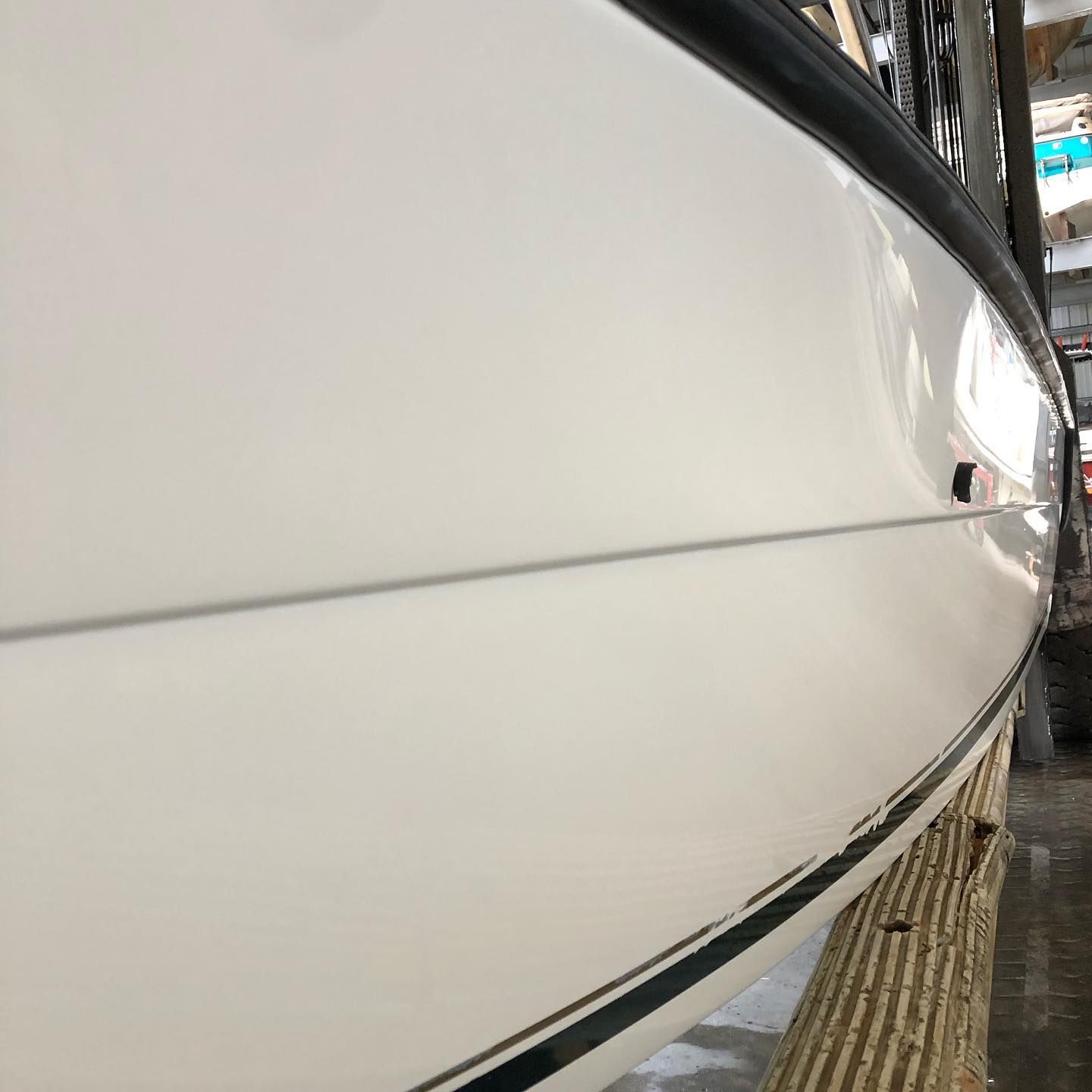 Close-up of a white boat hull with a black trim line, docked beside a wooden pier.
