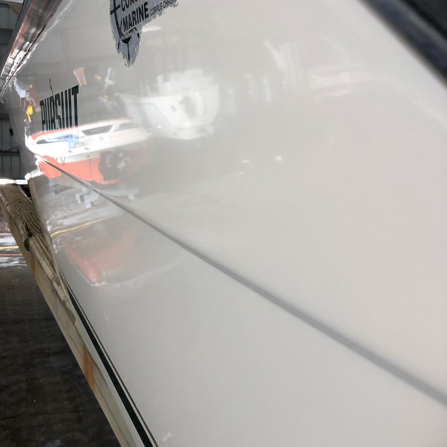 White boat hull with black lettering and reflections along a dockside walkway