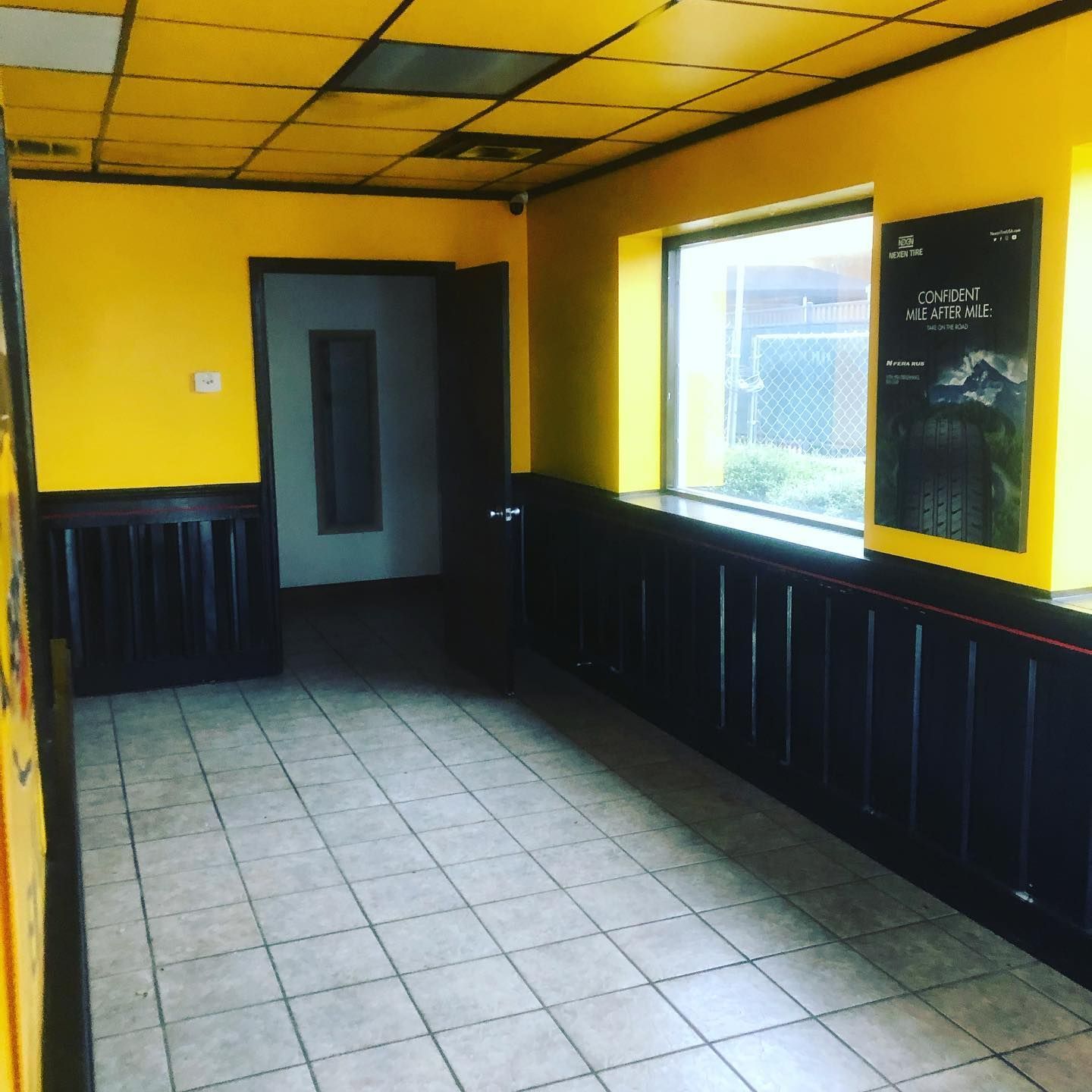 Empty yellow-and-black room with tiled floor, a window, door, and chalkboard on the right wall