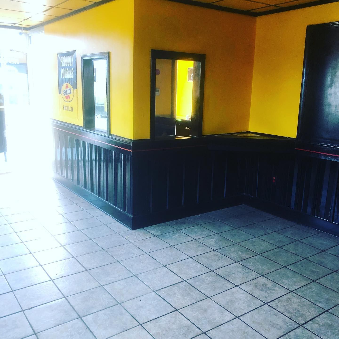Empty room with yellow walls, dark paneling, tiled floor, and a small window opening