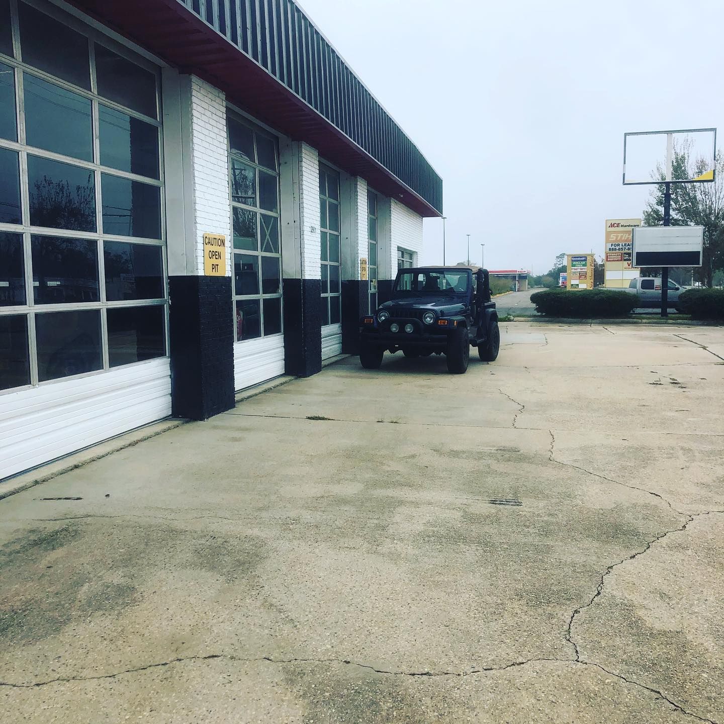 Black SUV parked beside a building with large garage windows on a cracked concrete lot
