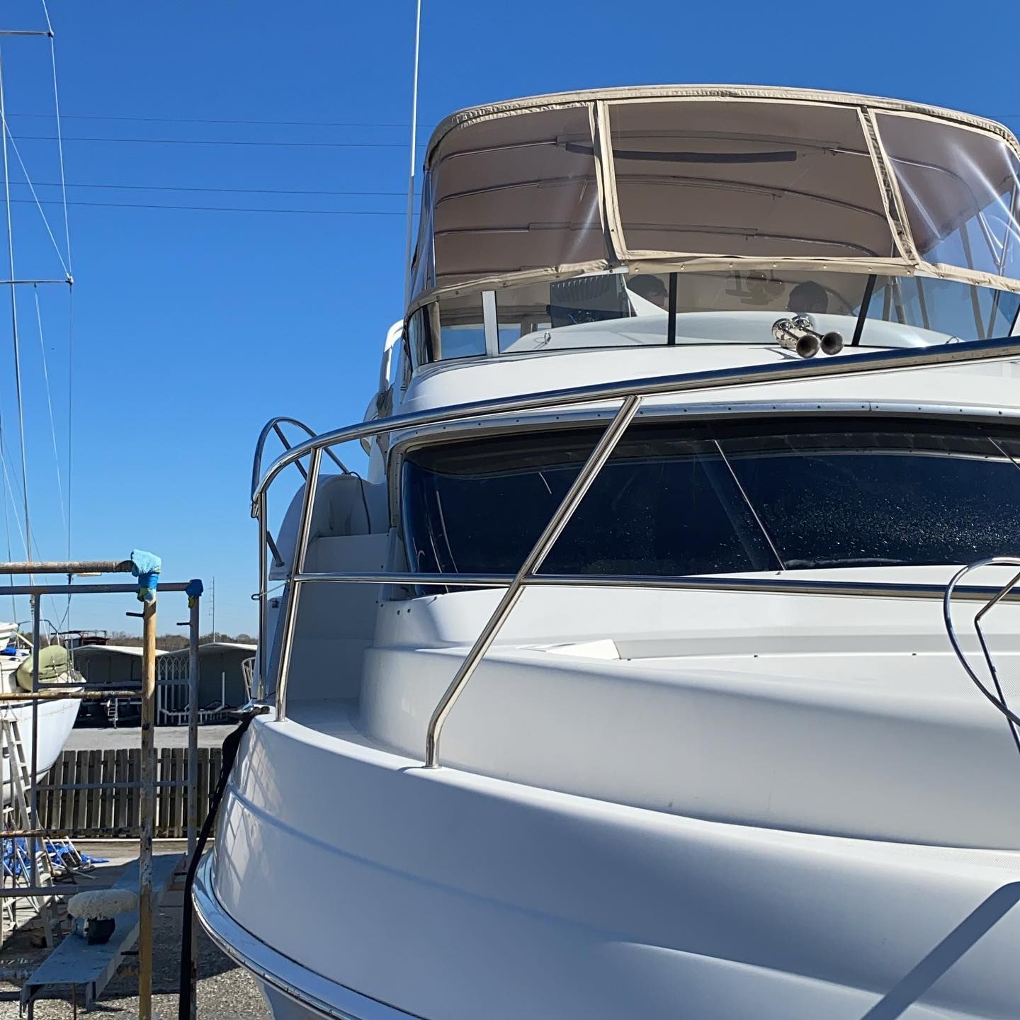 White motor yacht with a canopy docked at a marina under a clear blue sky