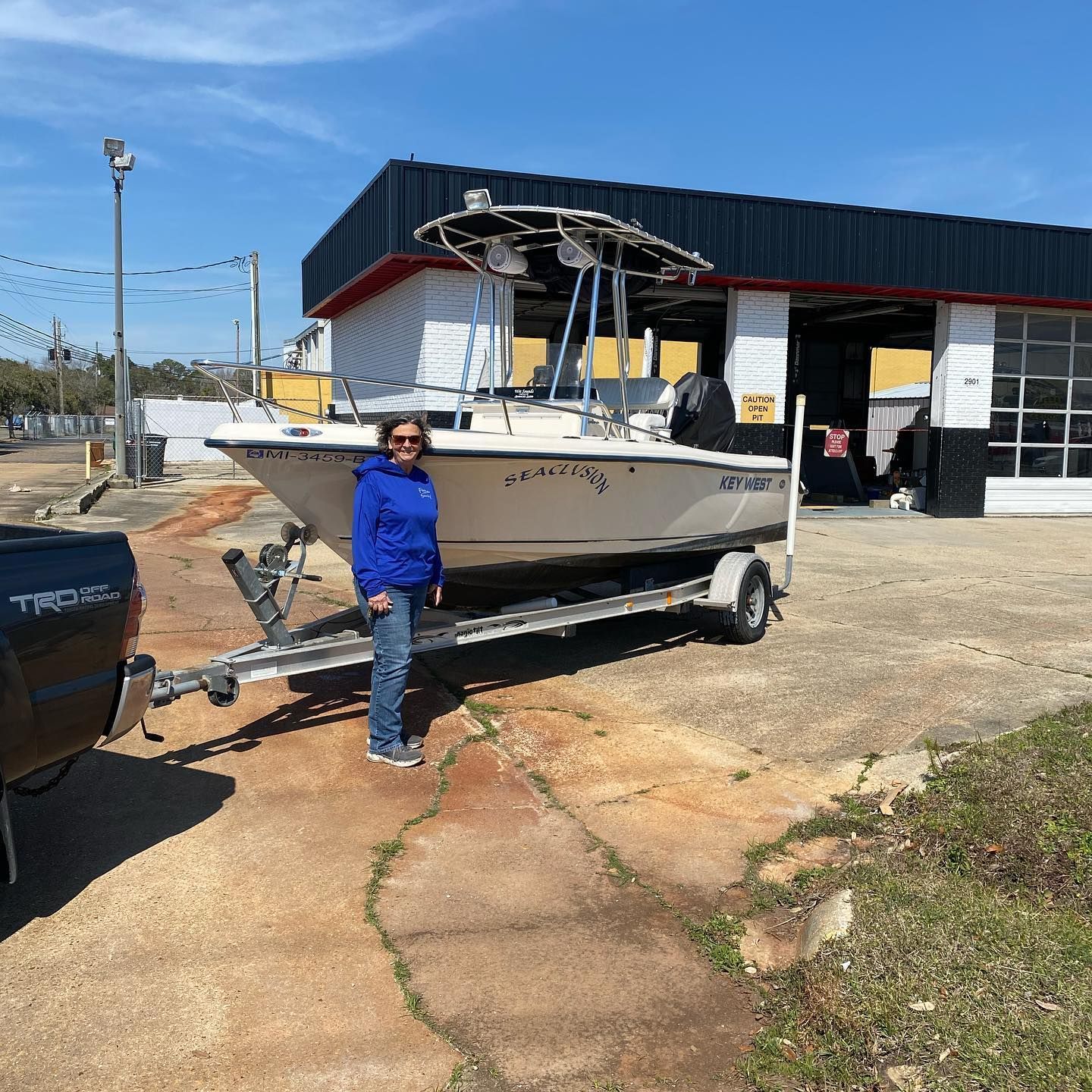 Person standing beside a boat on a trailer outside a building on a sunny day