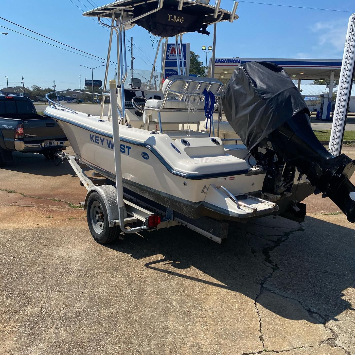 White Key West boat on a trailer with an outboard motor parked in a lot, under a canopy.