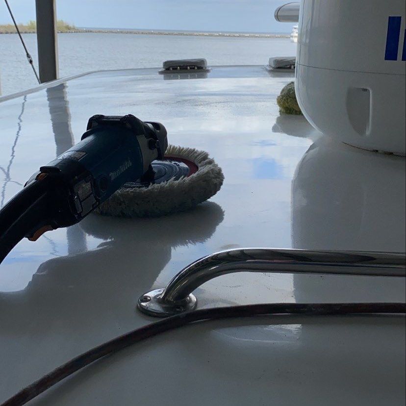 Close-up of a blue power tool on a boat deck beside a rope fender and rail in bright sunlight