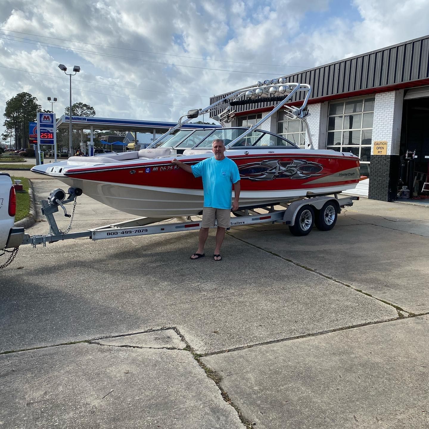 Man standing beside a red-and-white speedboat on a trailer outside a marina shop