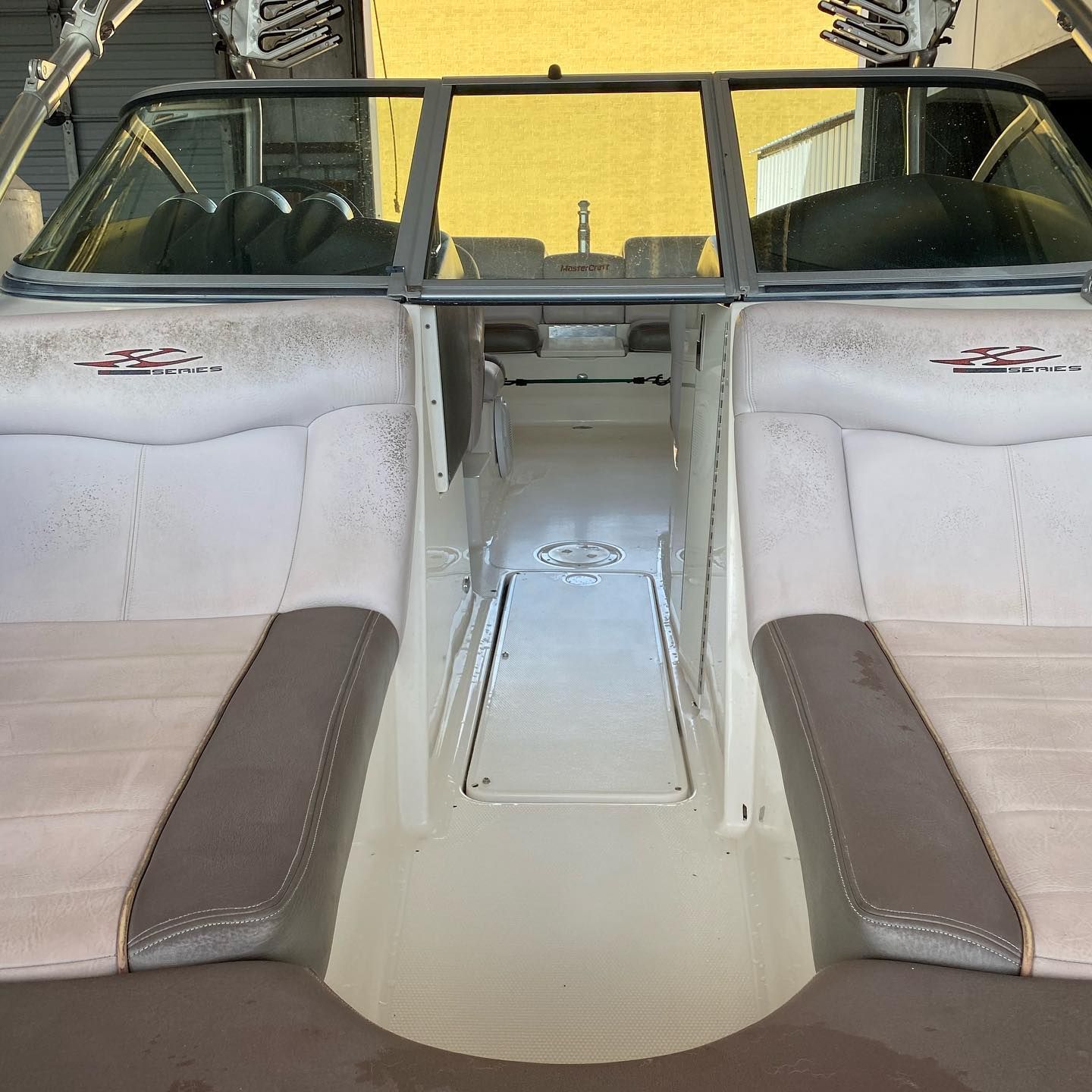 Boat interior with white and brown bench seats facing a central walkway and windshield frames.