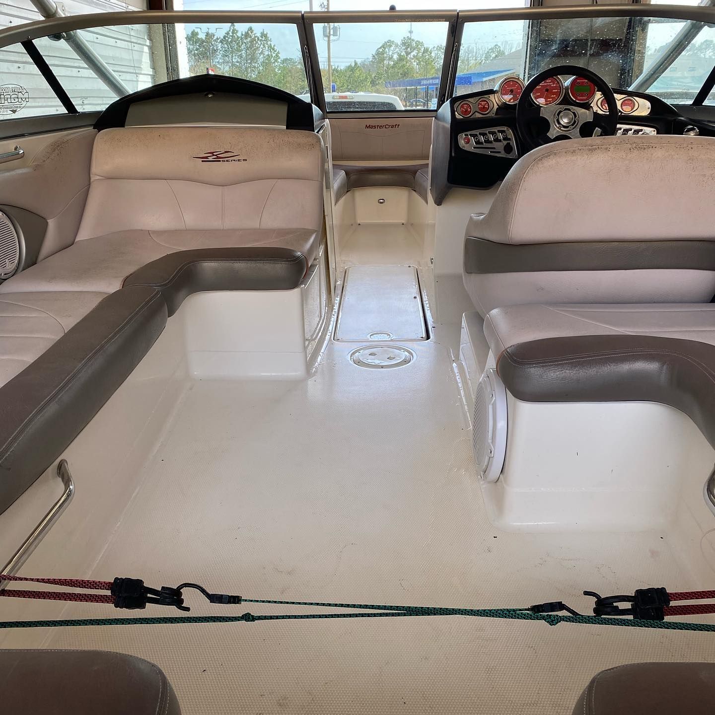 Boat cabin interior with beige bench seating, white floor, and steering wheel at the helm.
